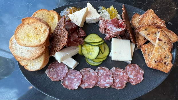 crostini, pickles, cheeses, cured meats and honeycomb on a black plate.