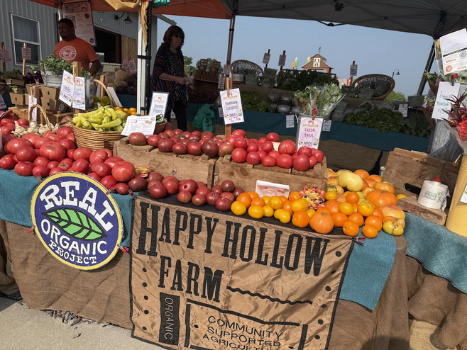 A colorful farmer's market booth with red and orange tomatoes in Columbia, Missouri, showcases local organic produce.