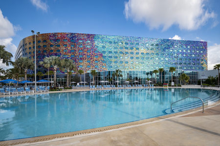 Large hotel pool with palm trees, beach chairs and a colorful hotel in the background at Universal Stella Nova Resort.