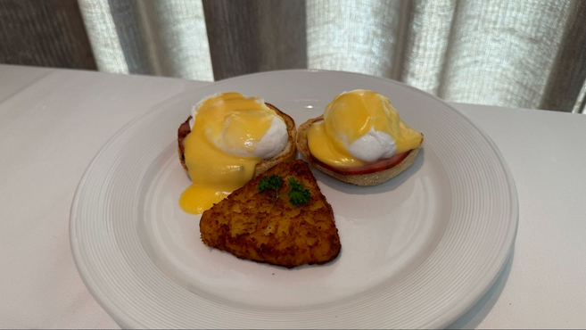 A white plate with eggs benedict and a triangle-shaped hash brown on top sitting on a white table cloth