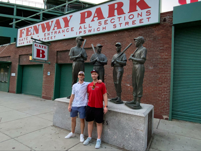 Two young guys standing in front of the Fenway monuments in Boston.