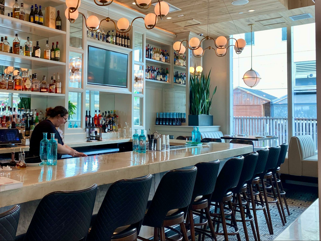 a lady bartender behind a long bar and black bar stools.