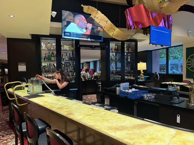 The Pineapple Bar and Bistro which features a long yellow bar and a glass case where various liquors are held.