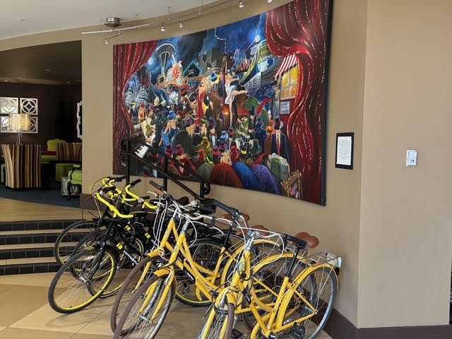 A row of six yellow bicycles which keep the pineapple theme going, stationed under a large colorful painting.