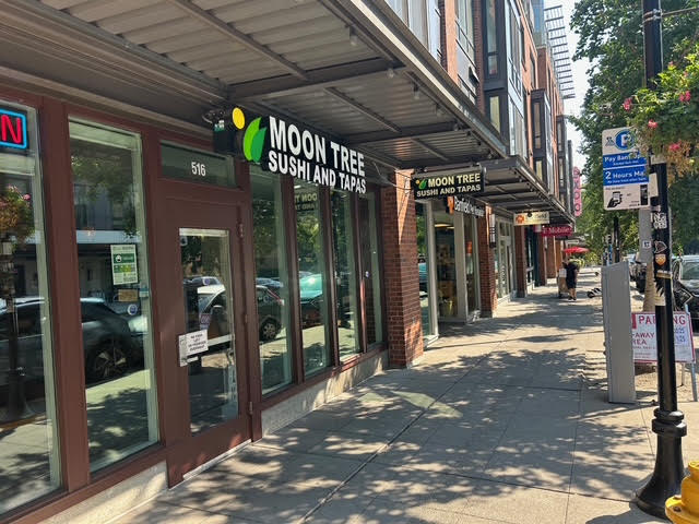 The front door of a nearby restaurant that serves sushi and tapas, with a lighted hanging sign that says, "The Moon Tree".