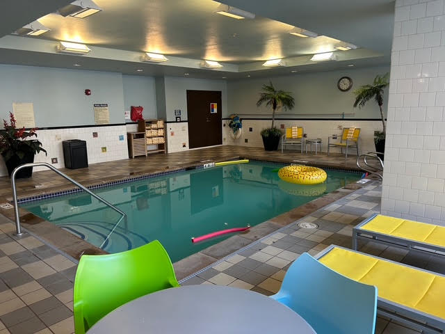 A swimming pool with a hand bar and steps leading into the water where pool noodles and an inner tube can be found.