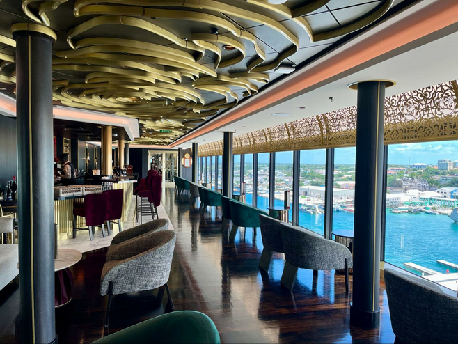 Disney Cruise Line's adult-exclusive lounge The Rose is pictured, with an ornate gold rose design on its ceiling, ample seating and floor-to-ceiling windows with stunning views of the ocean and Nassau in the Bahamas.