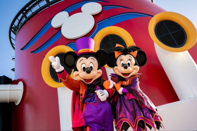 Mickey and Minnie Mouse pose in purple and orange Halloween costumes on the top deck of a Disney cruise ship.