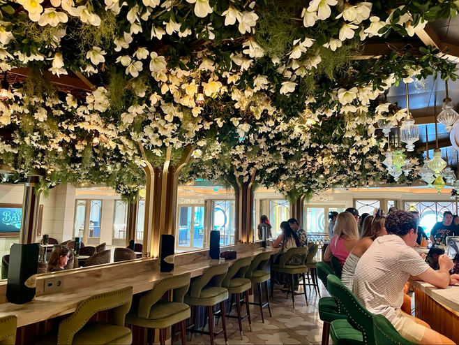 Guests sit at a bar in a Bayou-themed lounge (with a ceiling adorned with flowers and foliage) aboard a Disney cruise ship.