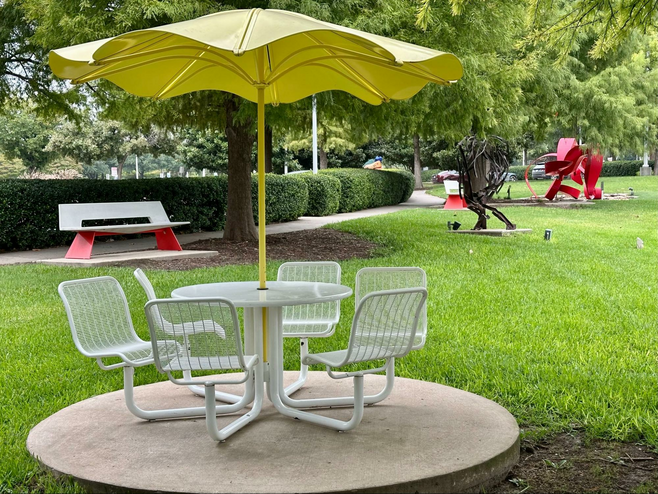 Umbrella-shaded outdoor table with a red sculpture in the background at the Texas Sculpture Garden.