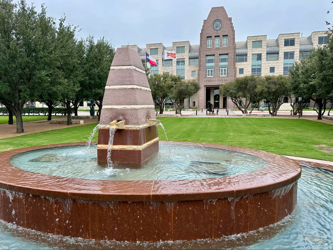 Frisco City Hall in Frisco Square with a large obelisk fountain in the foreground.