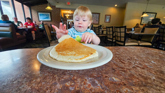 A toddler sitting at the Capital Pancake House with giant sized pancakes 