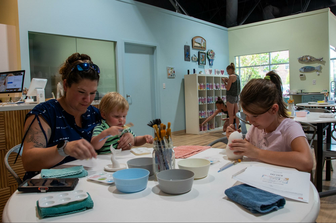 A mother and her two children sitting at a table painting ceramics 