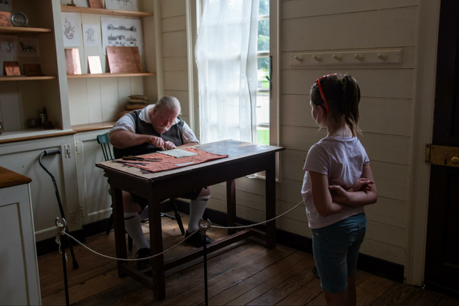A young girl watching a silversmith working in Colonial Williamsburg