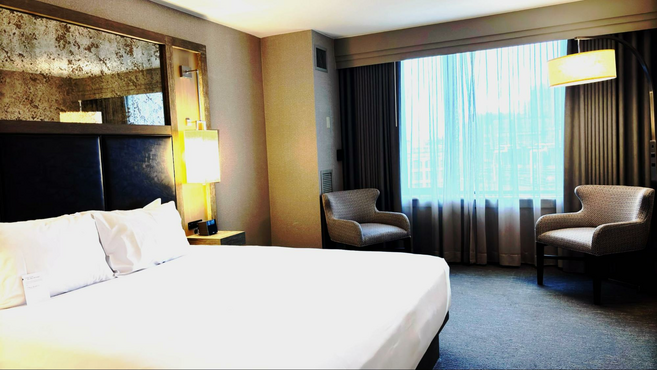 A king size bed with a nighttable and lamp next to it and two chairs by the window in an accessible room at the Hyatt Regency in Boston.
