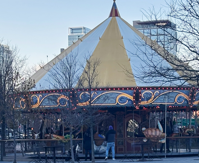 A Boston carousel topped with yellow and white, with kids riding it.