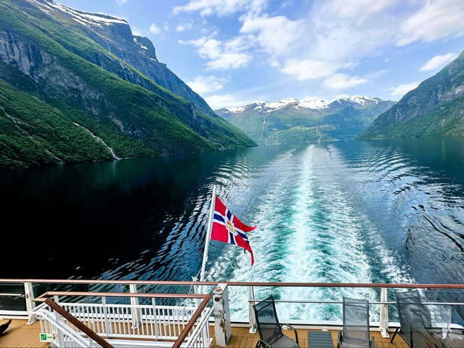 Norwegian flag flies on Pollux cruise ship sailing through fjord.