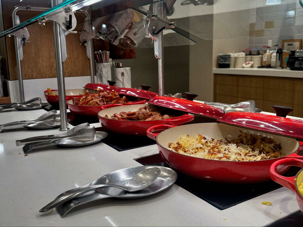 Eggs, bacon and hash browns in red serving dishes on buffet at Embassy Suites Austin daily breakfast. 