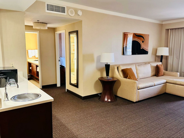 King suite living room and kitchenette at Embassy Suites Austin. The walls and furniture are beige with light brown accent pillows and artwork.
