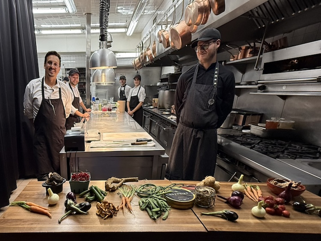 Head Chef Raphaël Vézina and his team greeting guests in the kitchen at Laurie Raphaël, with menu ingredients displayed, showcasing fine dining in Quebec City.