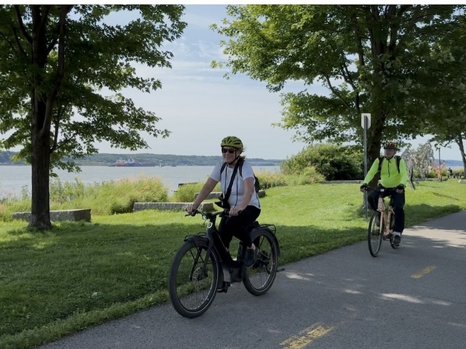 Traveler and guide on e-bikes along Promenade Samuel-de-Champlain by the St. Lawrence River, enjoying a scenic and romantic Quebec City experience.
