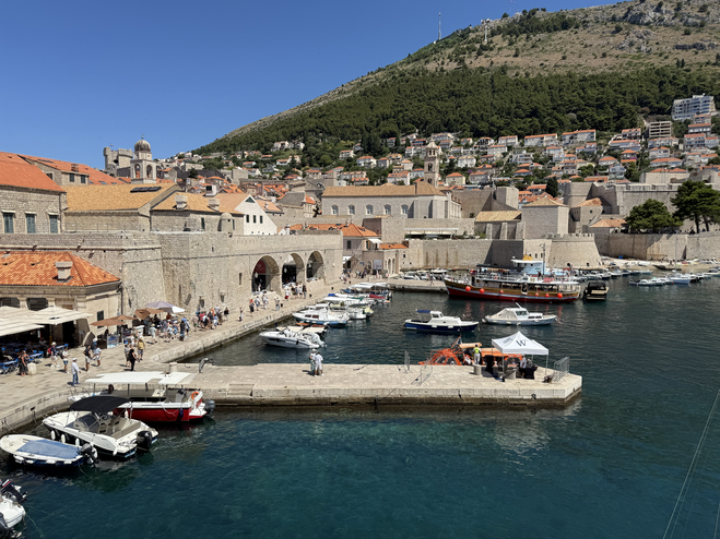 Looking out over Dubrovnik's historic Pile Harbor with small boats moored and city walls lining the harbor on Game of Thrones Tour.