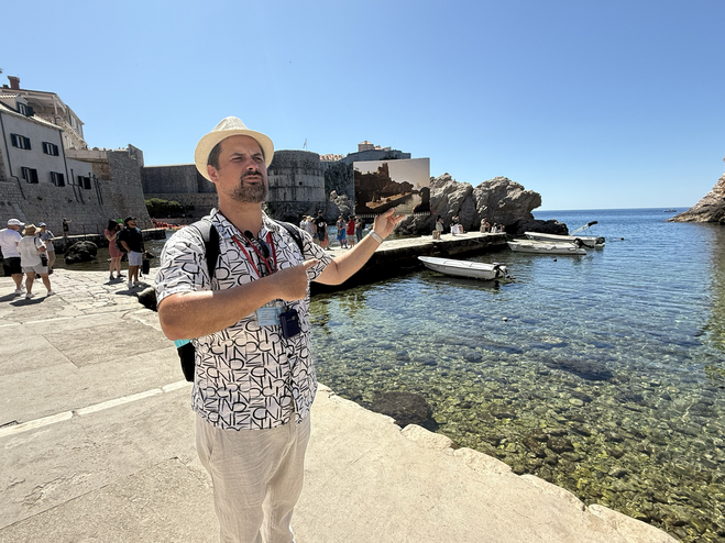 Tour guide holds up scene photo from Game of Thrones TV show so tourists can see how scenes were shot for show by Dubrovnik's Pile Harbor.