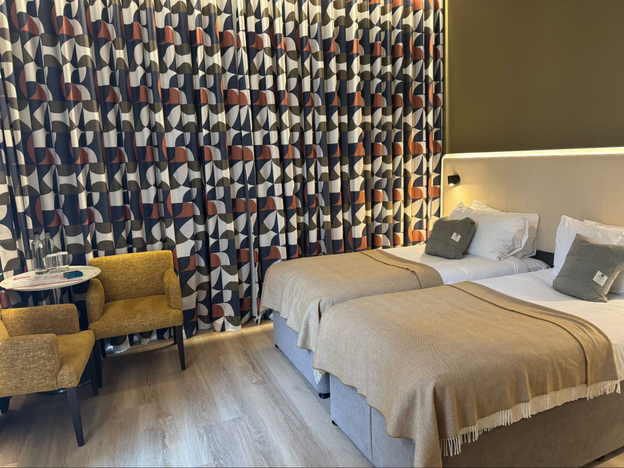 sunlight streams into twin-bed room at The Address Glasgow, funky curtain pattern and gold chairs in frame