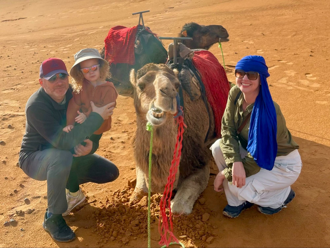 A family sits beside a camel in the Sahara desert of Morocco.