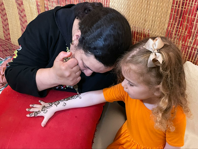 A young girl receives henna on her arm by an artist in Morocco.