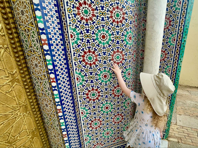 A young girl touches mosaic art on a building in Morocco.