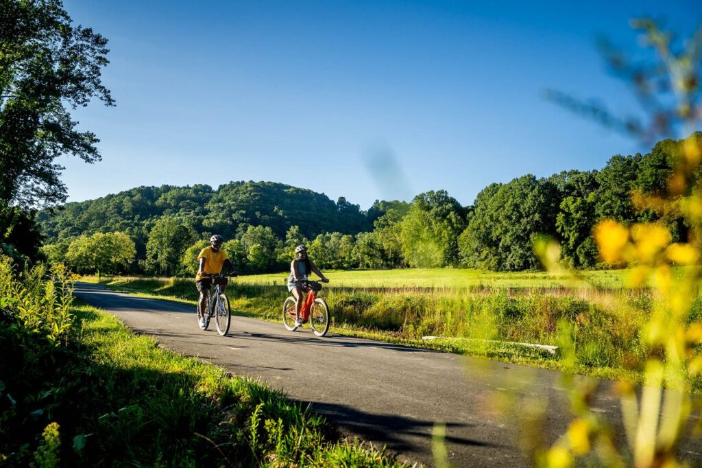2 people biking on the Ecusta Trail, a scenic route through rolling fields and tree covered hills, in Hendersonville NC