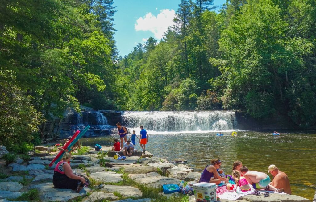 Families picnicking and playing in the cool waters at the base of Hooker Falls in the DuPont State Recreational Forest.