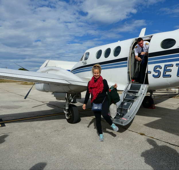 A woman in black with a red scarf exits the steps from a small jet airplane with the pilot peeking out from the door.