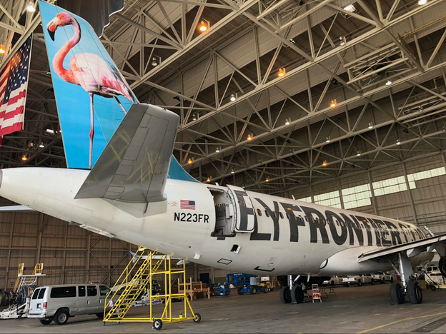 A Frontier Airlines airplane in the hanger with portable stairs and a van parked nearby.