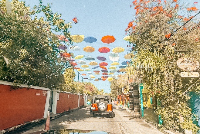 Red jeep rolling through the streets of Nassau with colorful umbrellas hanging from above
