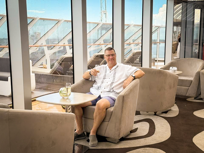 Man in white shirt and blue shorts drinking champagne in cruise ship lounge