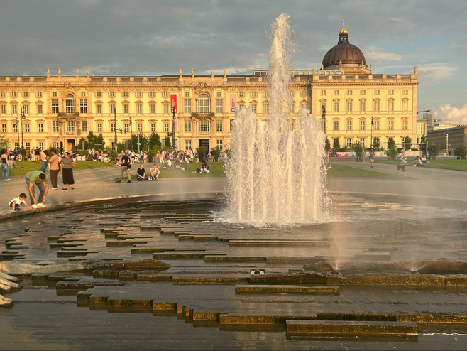 A view of the fountain and one of the museums on Berlin's famous Museum Island. Families and groups are relaxing on the grassy areas, enjoying the ambiance. 