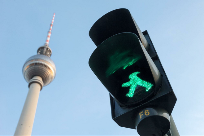 A picture of a Berlin traffic light with the green Ampelmännchen (little traffic light man) next to the city's landmark radio tower. 