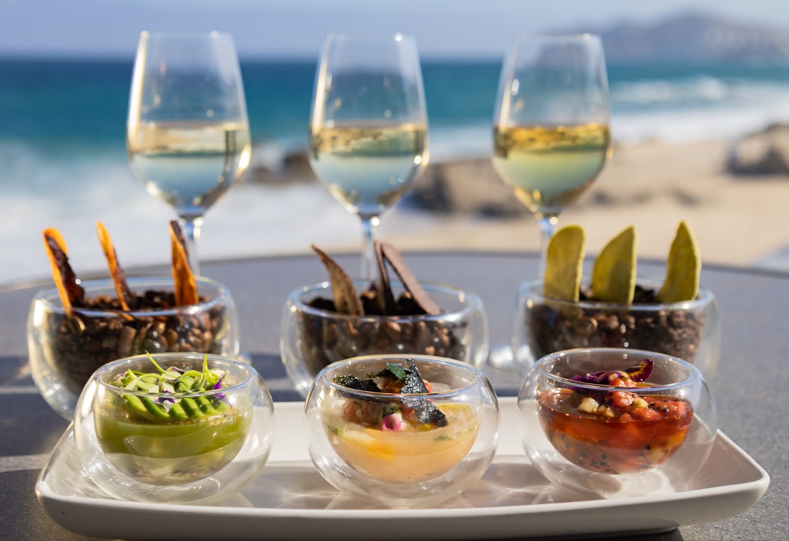 Three wine glasses with white wine, bowls of chips and dips and appetizers at Grand Velas Boutique Los Cabos adults-only all-inclusive resort