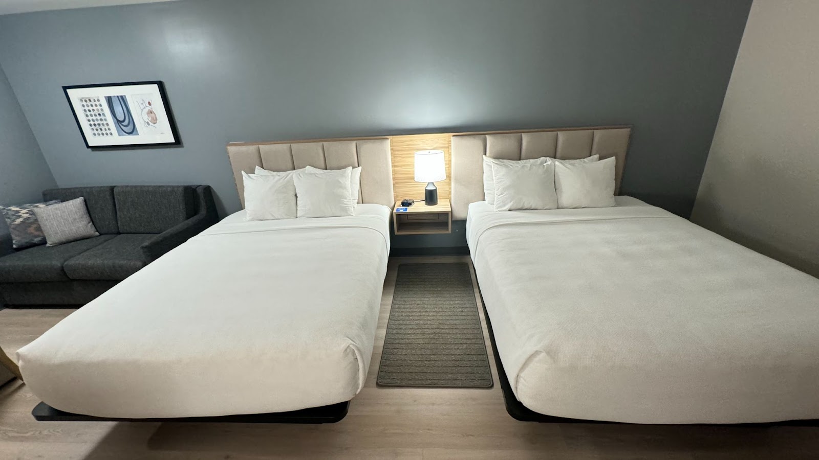 Two queen beds in a room with pillows propped up in front of a blue wall next to a sofa at Hyatt Studios Mobile Tillman's Corner