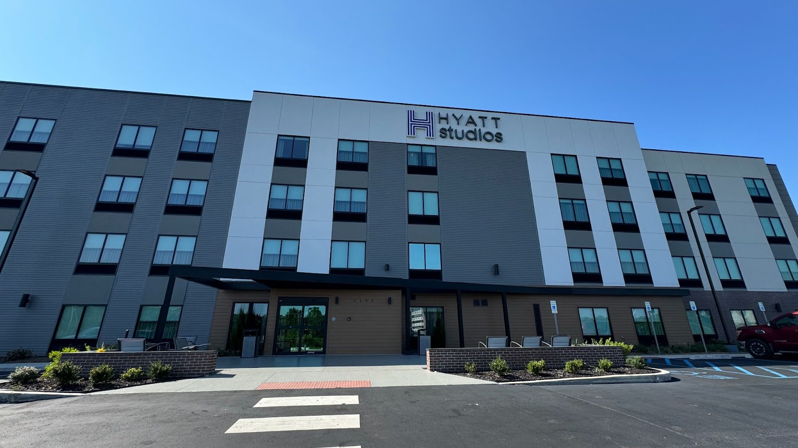 Exterior of grey and white hotel building with 15 windows and a crosswalk at Hyatt Studios Mobile Tillman's Corner