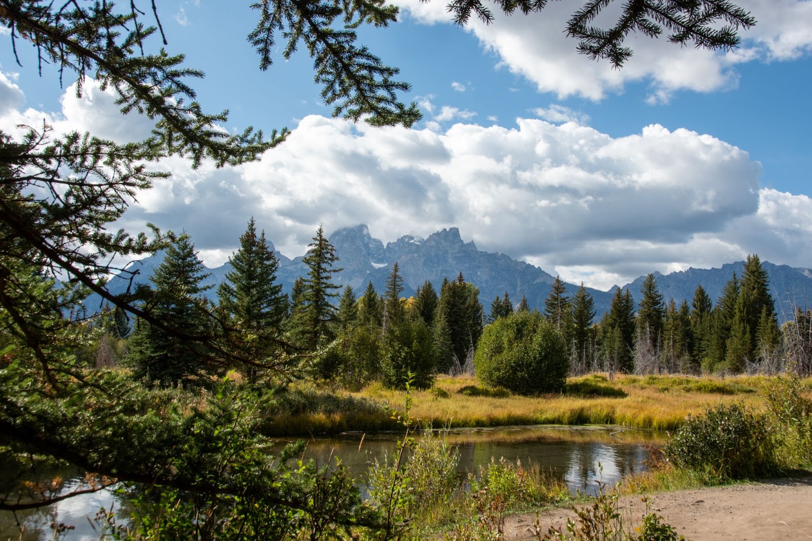 Bright blue sky with clouds around the mountain peaks with trees surrounding a lake
