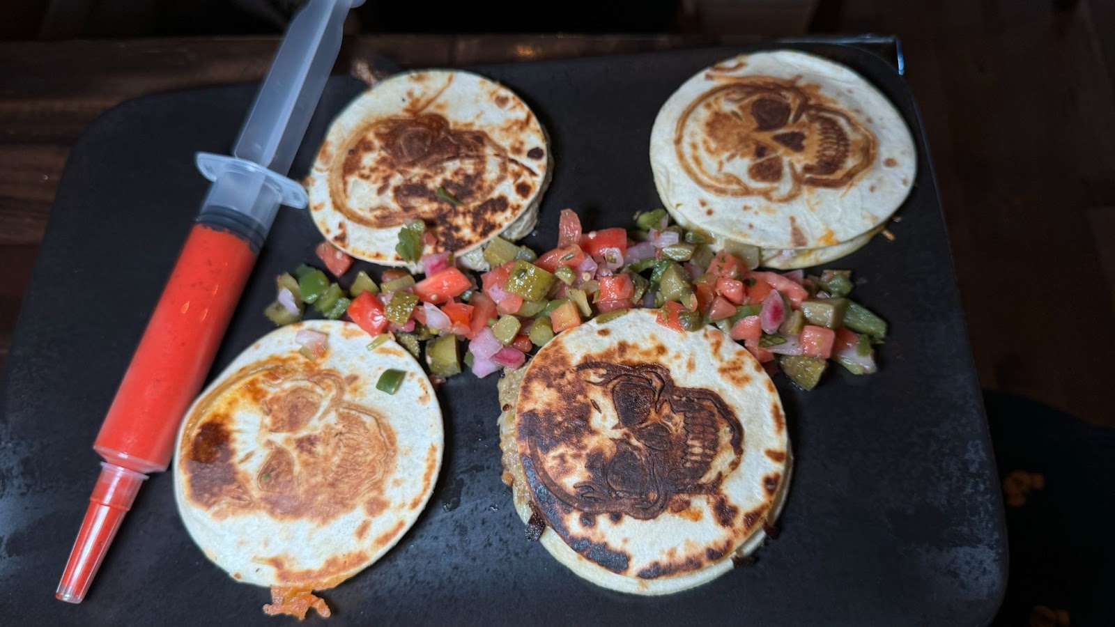 Tortillas with skeleton images on them next to a syringe of sauce on a black plate at Halloween bar in Orlando at Jock Lindsey's Halloween Hangar Bar.