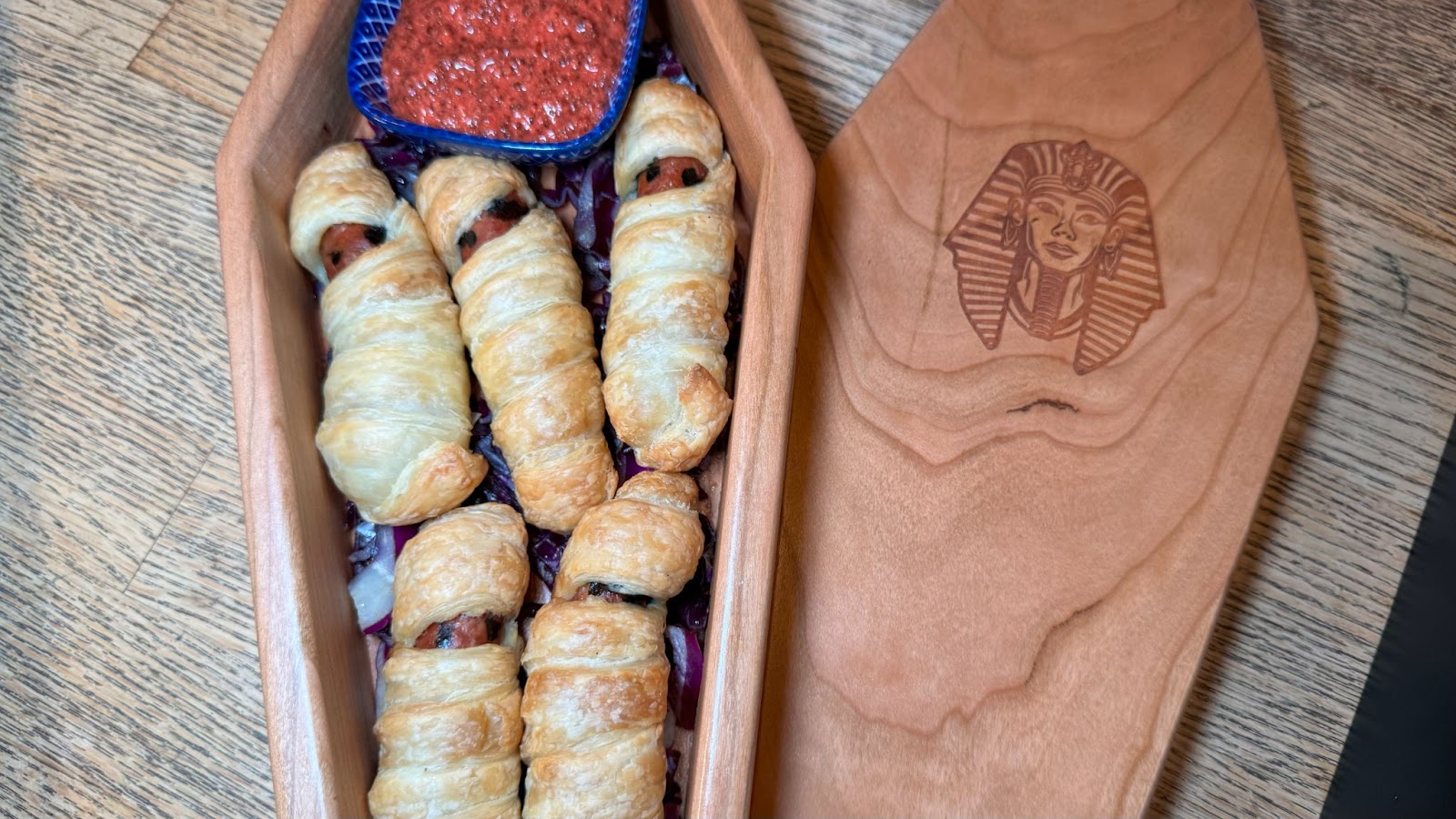 A tomb-shaped box filled with sausages next to a blue bowl filled with sauce at a Halloween bar in Orlando known as Jock Lindsey's Halloween Hangar Bar