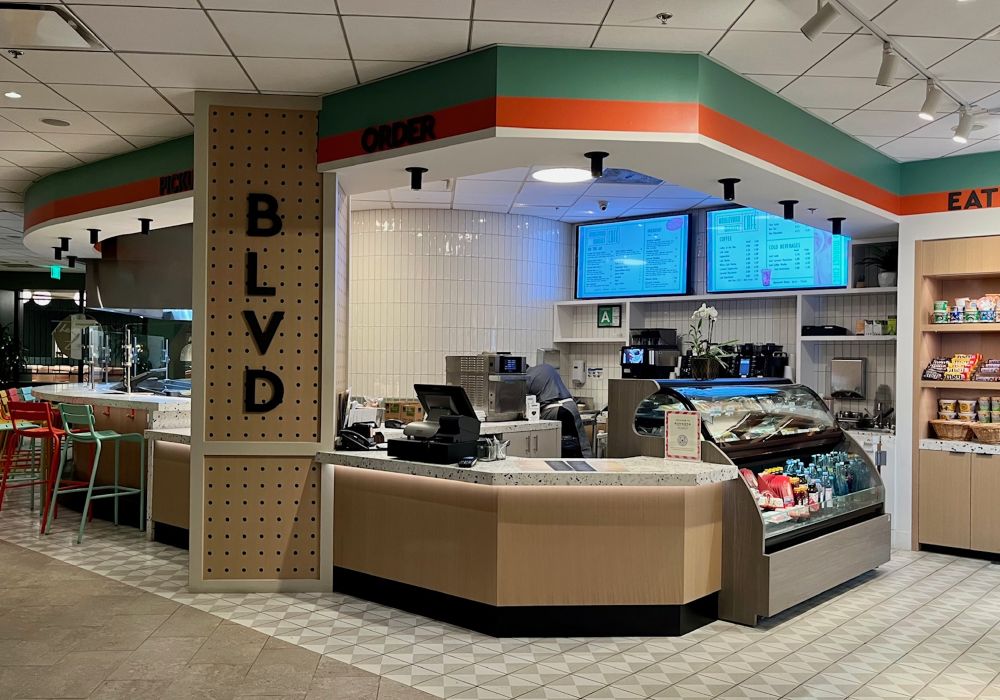 View of the Boulevard Cafe at the Sonesta Hotel LAX. A counter, menu screens, pastry display case and over to the side, a seating counter with tall stools.