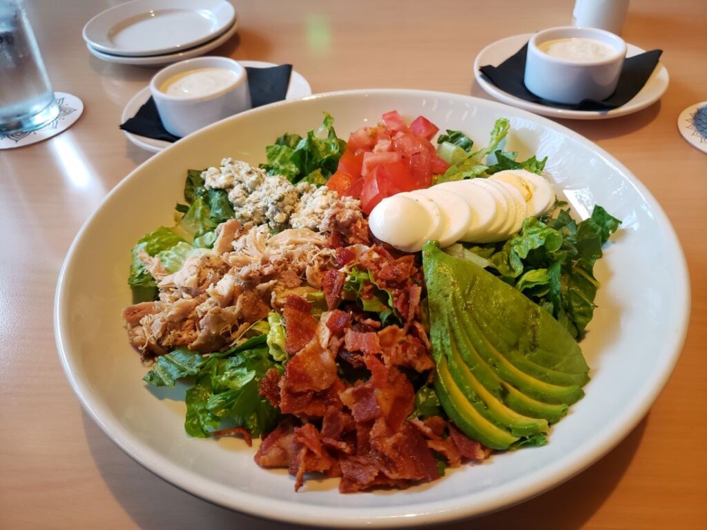 Cobb Salad, with dressing in white ramekins behind it.