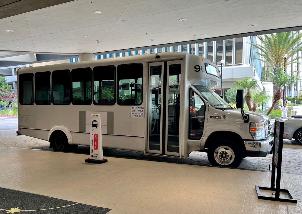 Small white shuttle bus parked under the overhang at the Sonesta Hotel LAX.