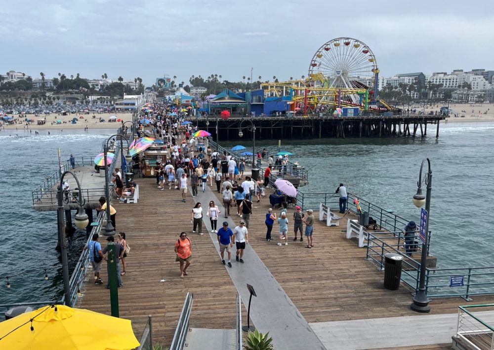 Image of the Santa Monica Pier, taken from the end of the pier looking toward the beach, with crowds and umbrellas on the pier and on the beach.