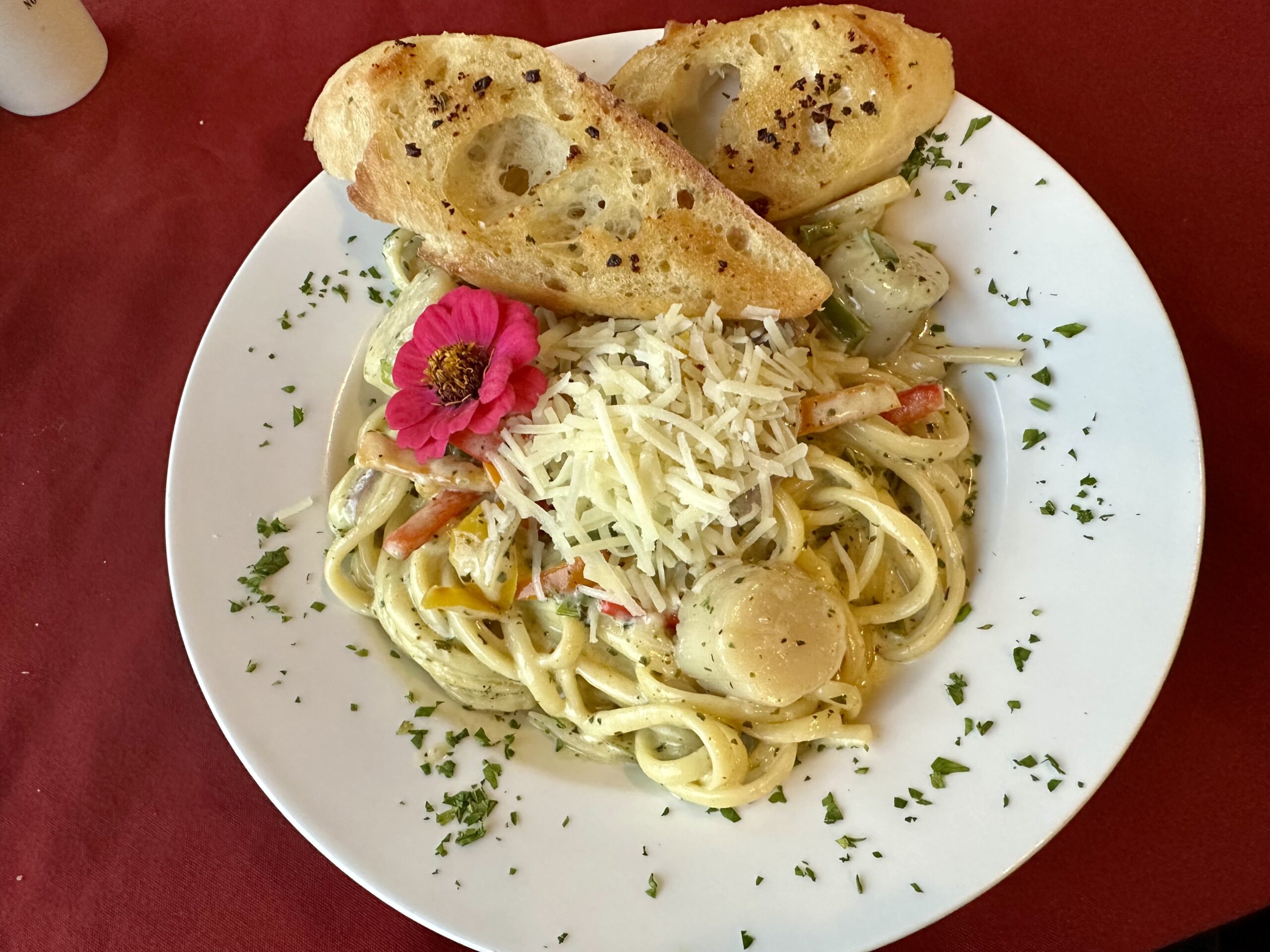 Scallops on pasta with a pink zinnia garnish and toasted baguettes at Train Station Inn Railway Dining Car in Tatamagouche, Nova Scotia.